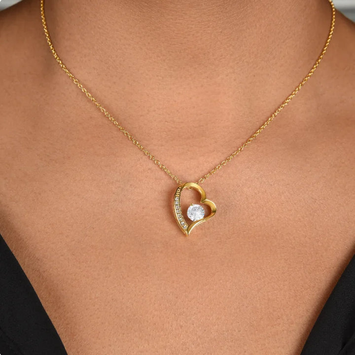 Gold heart-shaped necklace with a diamond pendant on a person's neck.