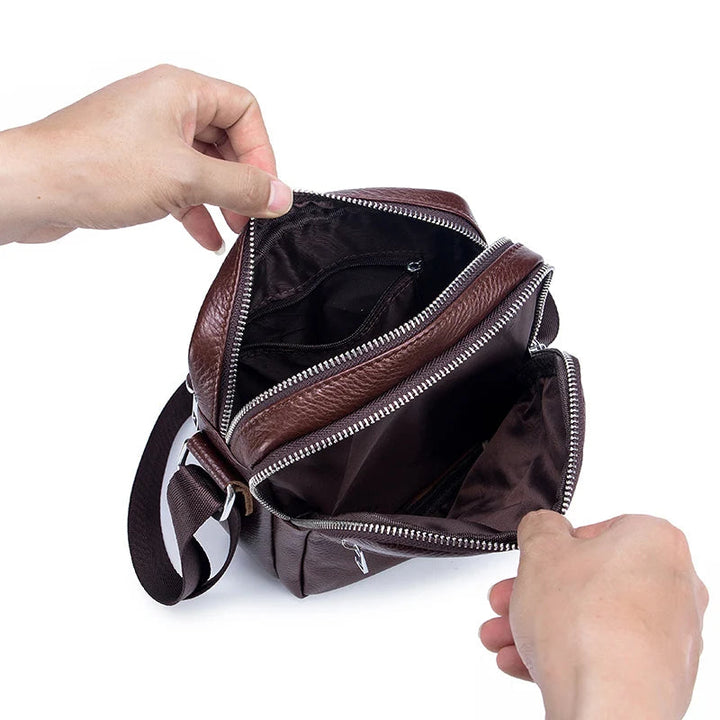 Brown leather bag with zippers being held open by a hand on a white background, with 'BULLCAPTAIN' brand visible.