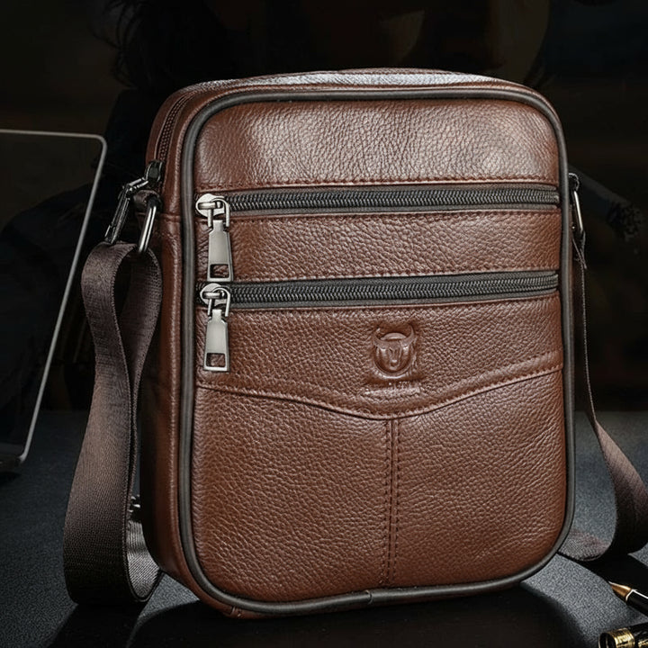 Brown leather crossbody bag with visible Bullcaptain logo on a dark background