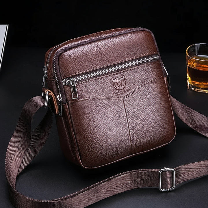 Brown leather crossbody bag with visible brand logo on a dark surface.