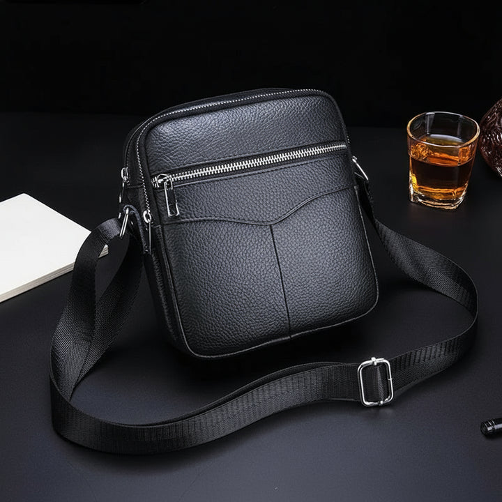 Black leather crossbody bag with a visible brand logo on a dark surface.