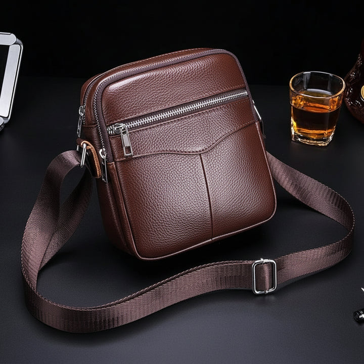 Brown leather crossbody bag with visible brand logo on a dark surface.