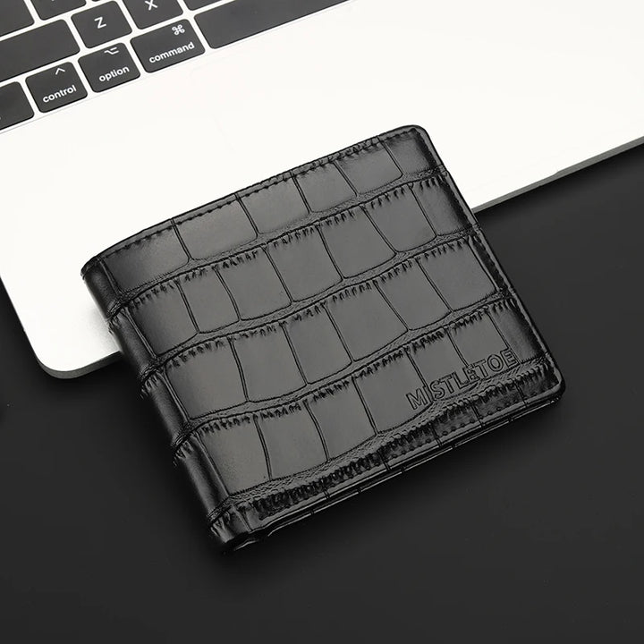 Black crocodile-patterned wallet on a dark surface with a laptop in the background